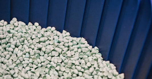 Small tear-drop shaped abrasive tumbling media inside a large blue finishing machine. The media is a light blue color.