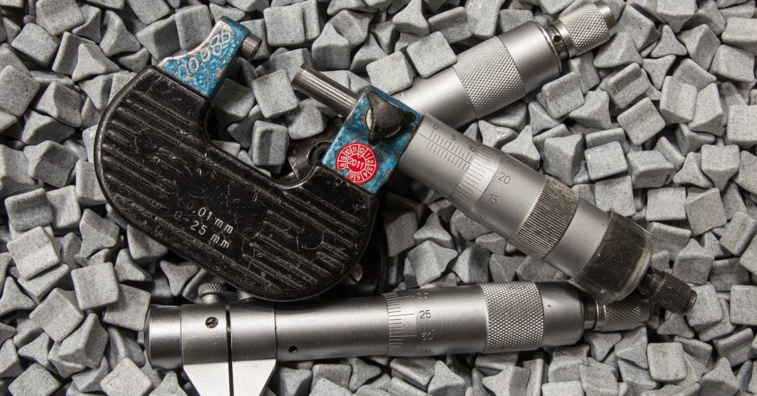 Three small metal parts lying on a pile of gray finishing media. The finishing media is shaped like a triangle.