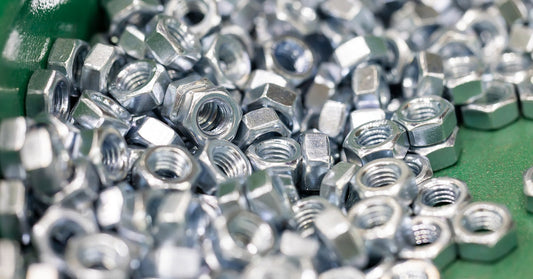 A large pile of shiny hex nuts sitting inside the tray of vibratory finishing machine. The finishing bowl is green.