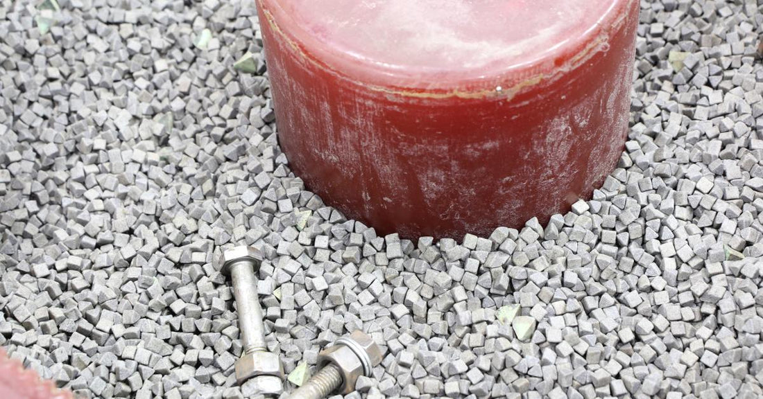 Two long metal fasteners inside a red vibratory finishing machine. The machine is full of small gray media.