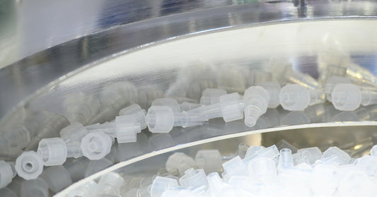 A vibratory finishing bowl in a brightly lit space. A pile of plastic translucent parts sits in the center of the bowl.